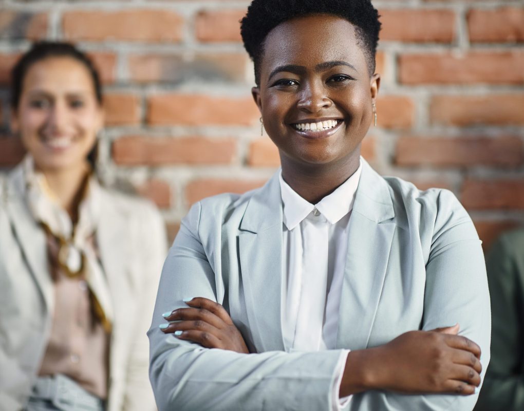 Confident African American female CEO standing with crossed arms in front of her business team and looking at camera.